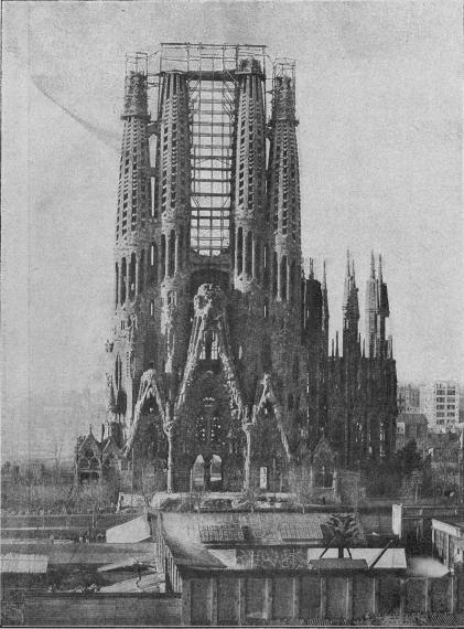 photographie en noir et blanc de la façade de la Nativité de la Sagrada Familia, vue de loin et en entier. Non achevée, il y a des échafaudages entre les tours et le bâtiment n'a pas encore d'autres murs.